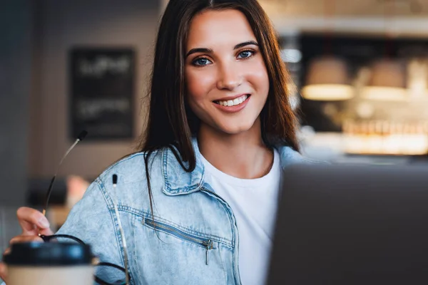 Vrouw lachend, kijkend naar de camera. Aantrekkelijke zakenvrouw zit aan tafel in de voorkant van laptop gesprekken op mobiele telefoon — Stockfoto