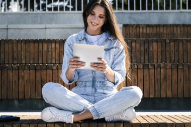 Milenyum kotlu kızı elinde akıllı bir tabletle parktaki bankta oturuyor. Kadın tablet kullanıyor