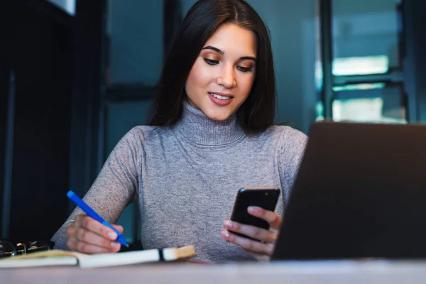 Attraktive forretningskvinner sitter ved bordet foran laptop, noterer i notatbok, utarbeider forretningsplan. – stockfoto