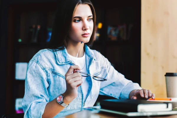 Vonzó üzletasszony ül az asztalnál a laptop előtt. Gyönyörű barna nő, kezében szemüveg — Stock Fotó