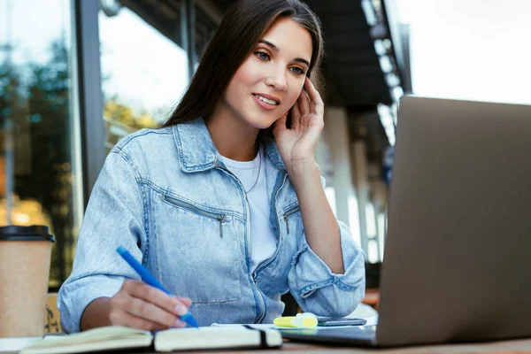 Joven mujer de negocios que trabaja en la terraza abierta en casa, sentada frente a la computadora portátil, sosteniendo el teléfono inteligente en su mano. — Foto de Stock