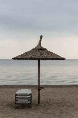 Reed şemsiye şezlong Sandy Beach ile. Şemsiye ve şezlong kasvetli hava ve sakin deniz. Reed şemsiye ve rahat koltuklar bulutlu gökyüzü arka plan üzerinde.
