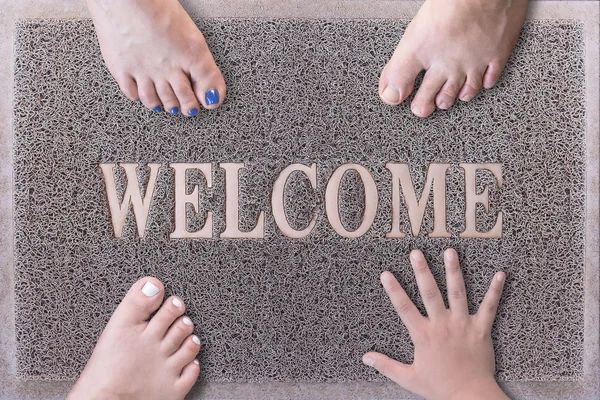 Welcome Door Mat With Three Feet and One Hand. Friendly Grey Door Mat Closeup with Bare Feet Standing. Welcome Carpet. Funny Three Feet and One Hand on Foot Scraper. — Stock Photo, Image