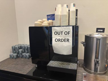 Arızalı kahve makinesi Danimarka 'nın iş yeri dinlenme yerinin ön panelinde el yazısıyla işaretlenmiş, düğmeleri ve şeker kutusuyla görünür durumda..