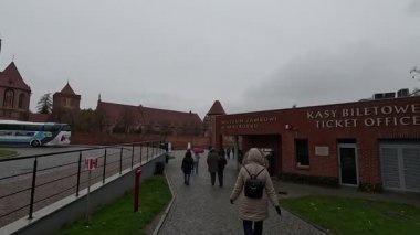 Polonya 'daki Malbork Kalesi' nin yağmurlu gündüz manzarası devasa tuğla duvarlar, Gotik kuleler ve bulutlu gökyüzünün altındaki Nogat Nehri 'ndeki hendekleri gösteriyor..