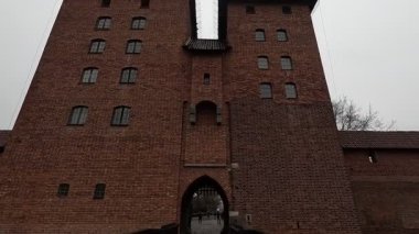 Polonya 'daki Malbork Kalesi' nin yağmurlu gündüz manzarası devasa tuğla duvarlar, Gotik kuleler ve bulutlu gökyüzünün altındaki Nogat Nehri 'ndeki hendekleri gösteriyor..