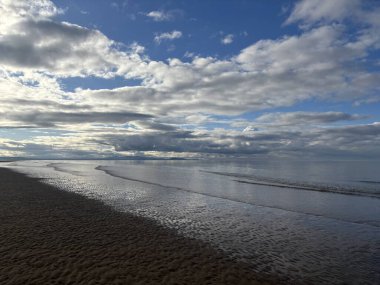 İskoçya 'daki Aberlady Körfezi' ndeki geniş kumlu sahil kum tepecikleri ve kıyıda hafif dalgalarla ovalanan ve haliçlerin üzerinde açık gökyüzü.