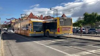 Lizbon, Portekiz 'de şehir sokaklarında hareket halindeki modern eklemli tramvayın dış görünüşü, geçen binalar, trafik ve kentsel çevre güzergahı boyunca.