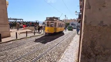 Lizbon, Portekiz 'deki dar kaldırımlı caddeler ve tepeler boyunca hareket halindeki klasik sarı tarihi tramvayın dış görünüşü, eski mimari ve şehir manzaralarını geçiyor..