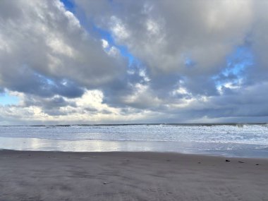 Fırtınalı bir günde İngiltere 'nin Northumberland kentindeki Bamburgh yakınlarındaki Ross Sands plajında dalgalı dalgalarla dalgalı deniz ve kara bulutlar..
