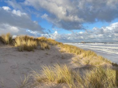 Fırtınalı bir günde İngiltere 'nin Northumberland kentindeki Bamburgh yakınlarındaki Ross Sands plajında dalgalı dalgalarla dalgalı deniz ve kara bulutlar..