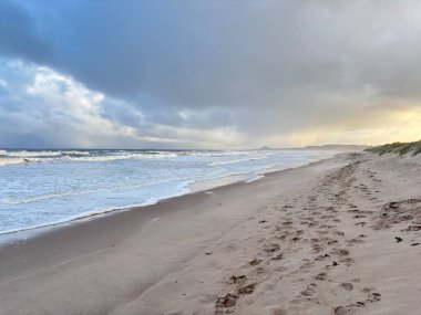 Fırtınalı bir günde İngiltere 'nin Northumberland kentindeki Bamburgh yakınlarındaki Ross Sands plajında dalgalı dalgalarla dalgalı deniz ve kara bulutlar..