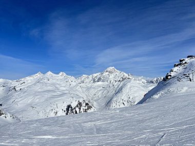 İtalya 'da Espace San Bernardo' nun bir parçası olan La Thuile kayak merkezindeki kayakçıları, kar kaplı binaları, sandalye kaldırıcıları, piste çıkanları, yamaçları ve dağ manzaralarını gösteren tatil kayak aktiviteleri