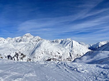 İtalya 'da Espace San Bernardo' nun bir parçası olan La Thuile kayak merkezindeki kayakçıları, kar kaplı binaları, sandalye kaldırıcıları, piste çıkanları, yamaçları ve dağ manzaralarını gösteren tatil kayak aktiviteleri