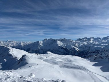 İtalya 'da Espace San Bernardo' nun bir parçası olan La Thuile kayak merkezindeki kayakçıları, kar kaplı binaları, sandalye kaldırıcıları, piste çıkanları, yamaçları ve dağ manzaralarını gösteren tatil kayak aktiviteleri
