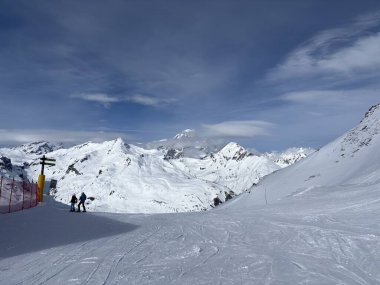 İtalya 'da Espace San Bernardo' nun bir parçası olan La Thuile kayak merkezindeki kayakçıları, kar kaplı binaları, sandalye kaldırıcıları, piste çıkanları, yamaçları ve dağ manzaralarını gösteren tatil kayak aktiviteleri