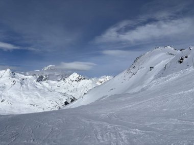 İtalya 'da Espace San Bernardo' nun bir parçası olan La Thuile kayak merkezindeki kayakçıları, kar kaplı binaları, sandalye kaldırıcıları, piste çıkanları, yamaçları ve dağ manzaralarını gösteren tatil kayak aktiviteleri