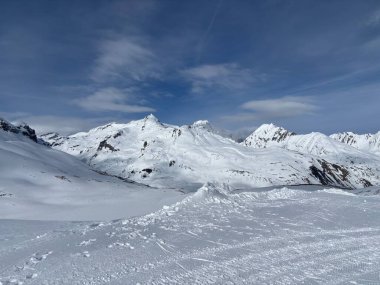 İtalya 'da Espace San Bernardo' nun bir parçası olan La Thuile kayak merkezindeki kayakçıları, kar kaplı binaları, sandalye kaldırıcıları, piste çıkanları, yamaçları ve dağ manzaralarını gösteren tatil kayak aktiviteleri