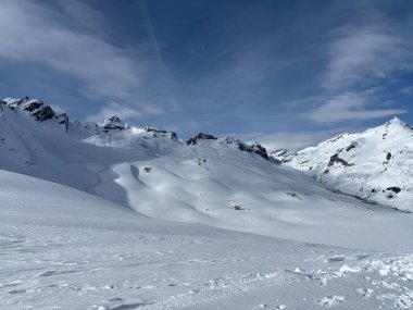 İtalya 'da Espace San Bernardo' nun bir parçası olan La Thuile kayak merkezindeki kayakçıları, kar kaplı binaları, sandalye kaldırıcıları, piste çıkanları, yamaçları ve dağ manzaralarını gösteren tatil kayak aktiviteleri