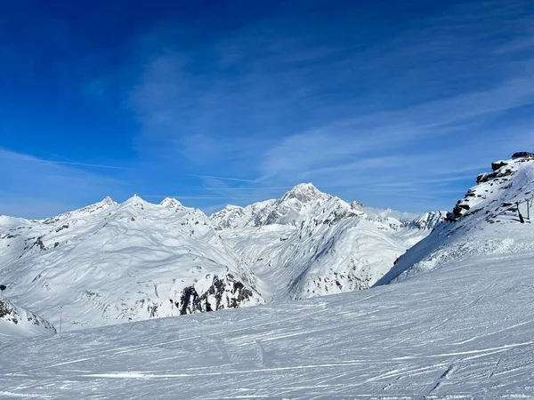 İtalya 'da Espace San Bernardo' nun bir parçası olan La Thuile kayak merkezindeki kayakçıları, kar kaplı binaları, sandalye kaldırıcıları, piste çıkanları, yamaçları ve dağ manzaralarını gösteren tatil kayak aktiviteleri