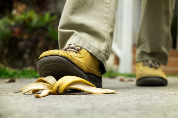 Men foot in a yellow shoe stepping on banana peel