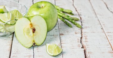 beyaz ahşap masa üzerinde yeşil elma, kireç ve kuşkonmaz