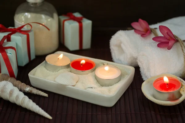 White towels, seashells and candles in sand with gift boxes