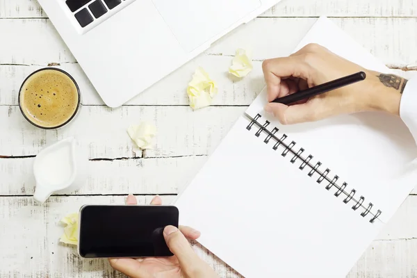 Woman hands holding phone and writing note over office desk