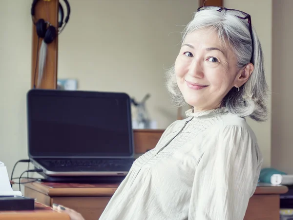 Азіатський жінка старший відхилився назад в її стілець і посміхається — стокове фото