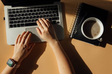 Dizüstü bilgisayarda çalışan bir kadın. Masasında bir fincan kahve ve defter var.
