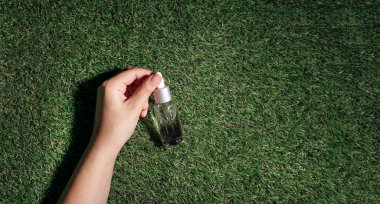 Kırpılmış el yapımı, şeffaf damlatan şişeyi serum losyonuyla ya da çimenlerin üzerinde gerekli yağla tutarken. Cilt bakımı kozmetik kavramı.