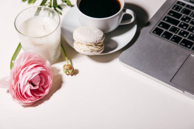 Beyaz masadaki badem kurabiyesi, mum, çiçek ve dizüstü bilgisayarlı kahvenin yakın plan görüntüsü.