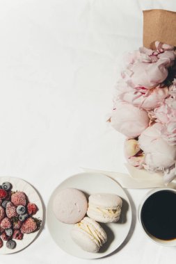 Beyaz arka planda bir fincan kahve, böğürtlen, badem kurabiyesi ve şakayık çiçeği.  