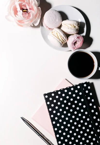 Bir fincan kahve, defterler, kalem, badem kurabiyeleri ve beyaz arka planda şakayık çiçekleri. 