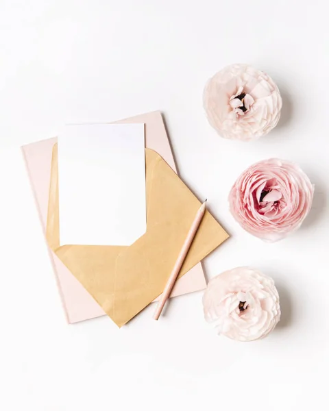 Üzerinde pembe çiçekler ve beyaz arka planda boş bir kart olan bir zarf. düz yatış, üst görünüm.
