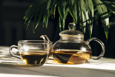 Ahşap masa arkasındaki cam bardak ve çaydanlığın yakın plan görüntüsü.