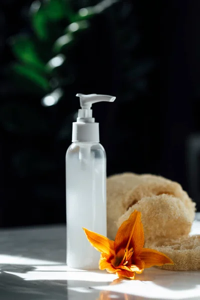 Bottle of cosmetic product and flower on a natural background.