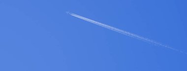 Beyaz uçak mavi gökyüzünde uçar arkasında bulutlardan oluşan bir iz bırakır.