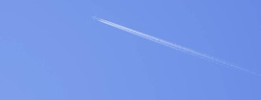 Beyaz uçak mavi gökyüzünde uçar arkasında bulutlardan oluşan bir iz bırakır.