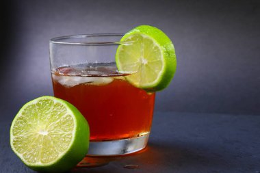 Buzlu bir bardakta servis edilen ferahlatıcı bir buzlu çayın yakın çekimi ve kenarında koyu arkaplanda izole edilmiş taze limon dilimi..