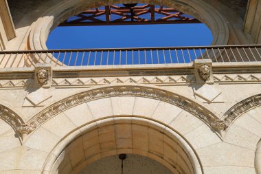 Kaya kemerleri, dekoratif oymalar ve berrak mavi gökyüzü altında klasik mimari unsurlar bulunan zarif tarihi bir binanın ön yüzü..