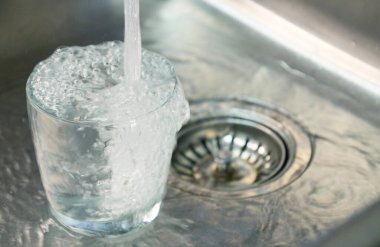 Temiz bardaklar, paslanmaz çelik lavaboda taze musluk suyuyla dolduruluyor. Temizliği, suyu, ev ortamını ve güvenli içme suyu konseptini simgeliyor..