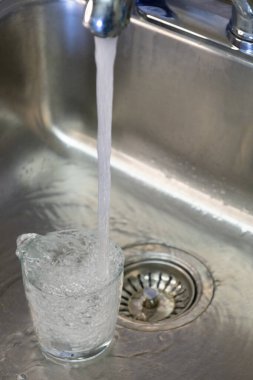 Temiz bardaklar, paslanmaz çelik lavaboda taze musluk suyuyla dolduruluyor. Temizliği, suyu, ev ortamını ve güvenli içme suyu konseptini simgeliyor..