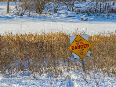 Donmuş nehir ya da kışın gölet yakınında ince buz olduğuna dair uyarı işareti. Karlı zemin, soğuk hava koşulları, mevsimsel güvenlik kavramı açık hava.