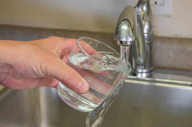 Bardaktan akan temiz musluk suyunu akan musluğun yanındaki mutfak lavabosuna boşaltan elin yakın çekimi. Su kullanımı, atık, ev hizmetleri, hijyen ve çevre kavramı.