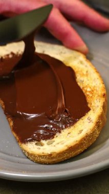 Metal bıçaklı tost ekmeğine çikolata serpiştiren kişi, gri tabak arka planı, kahvaltı ve tatlı konsepti, yakın plan yemek hazırlama.