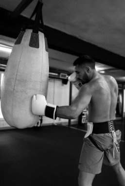 Spor salonunda torbayı yumruklayan bir boksörün siyah beyaz fotoğrafı.