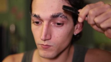 man combing his eyebrows upwards, applying drag make-up