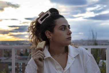 Caucasian woman eating a cookie during sunset on balcony