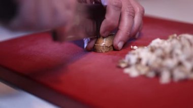 Bir adamın elleri mutfakta kırmızı bir kesme tahtasıyla mantar kesiyor.